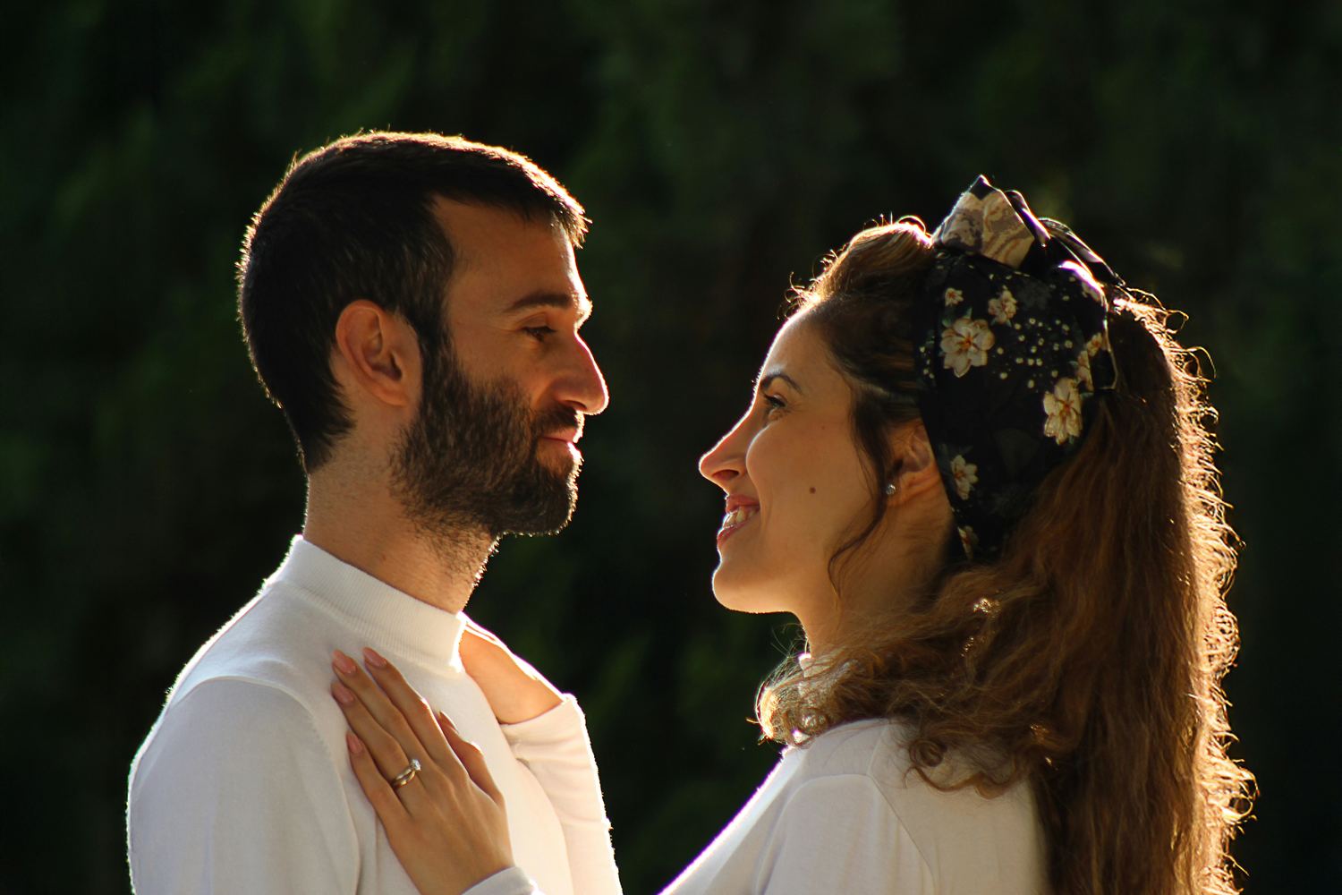 A young Israeli couple stands face to face, smiling, in warm evening light.
